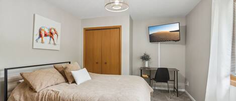 A bedroom with a bed, a desk, a television, and a door.