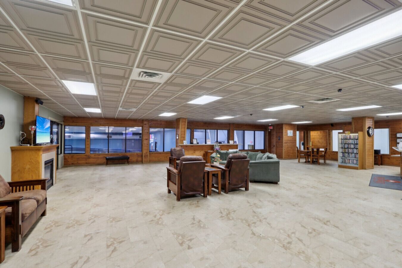 A spacious lobby with a high ceiling, wooden walls, and a fireplace. There are several seating areas with couches and chairs, and a large window offering a view outside.