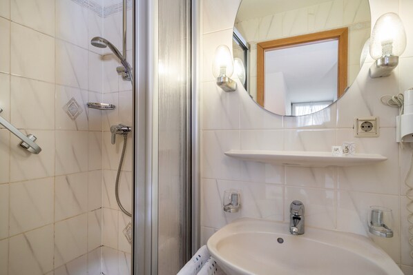 A bathroom with a shower, sink, mirror, and light fixtures.