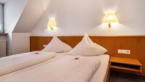 Een kamer met twee bedden, elk met een kussen en een nachtkastje. Er zitten wandlampen aan het plafond.