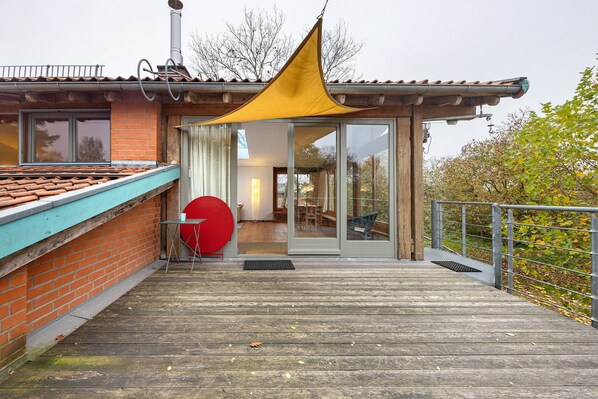 A wooden deck with a yellow canopy, a red circular object, and a glass door leading to an interior space.