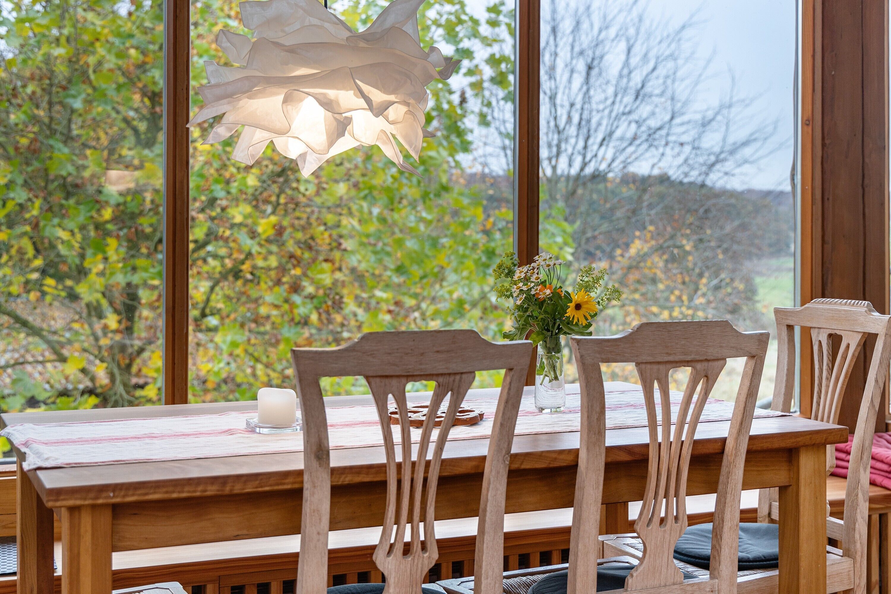 A wooden dining table with chairs, a vase with flowers, and a candle.