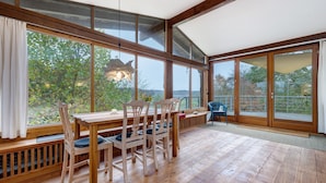Un espace repas avec des meubles en bois, de grandes fenêtres et une vue sur la verdure.