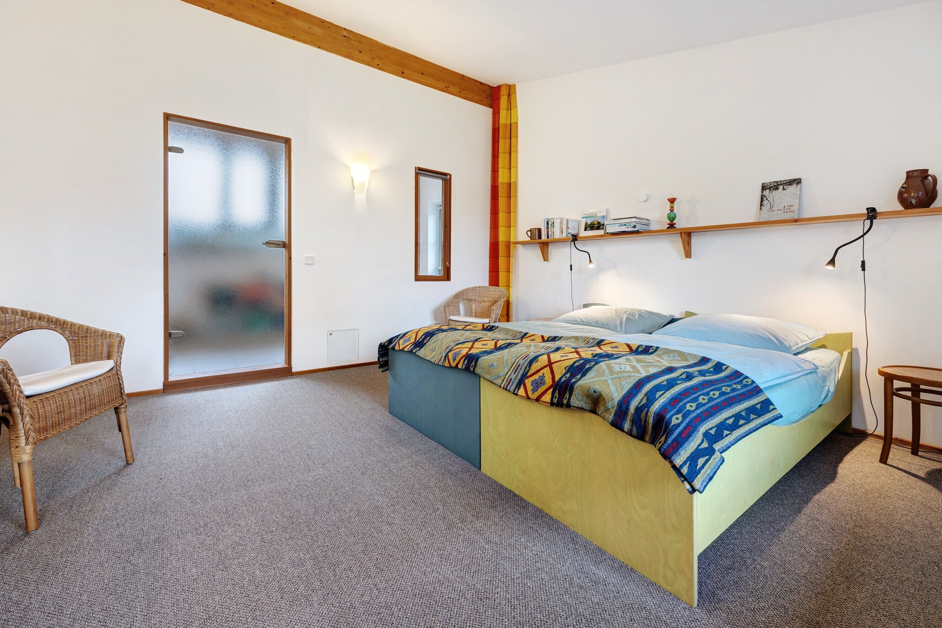 A bedroom with a bed, a chair, a shelf with items, and a door.