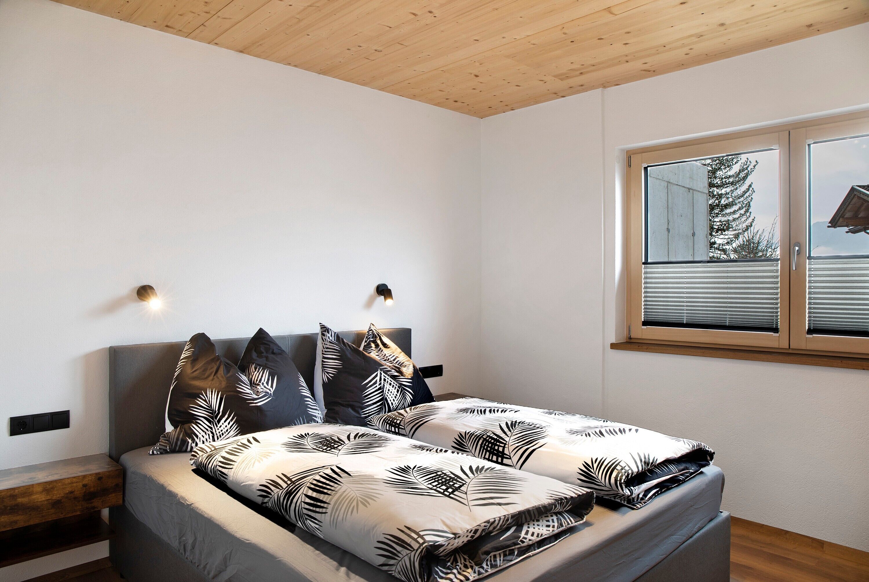 A bedroom with a bed, a nightstand, a wall-mounted light, and a window with blinds.