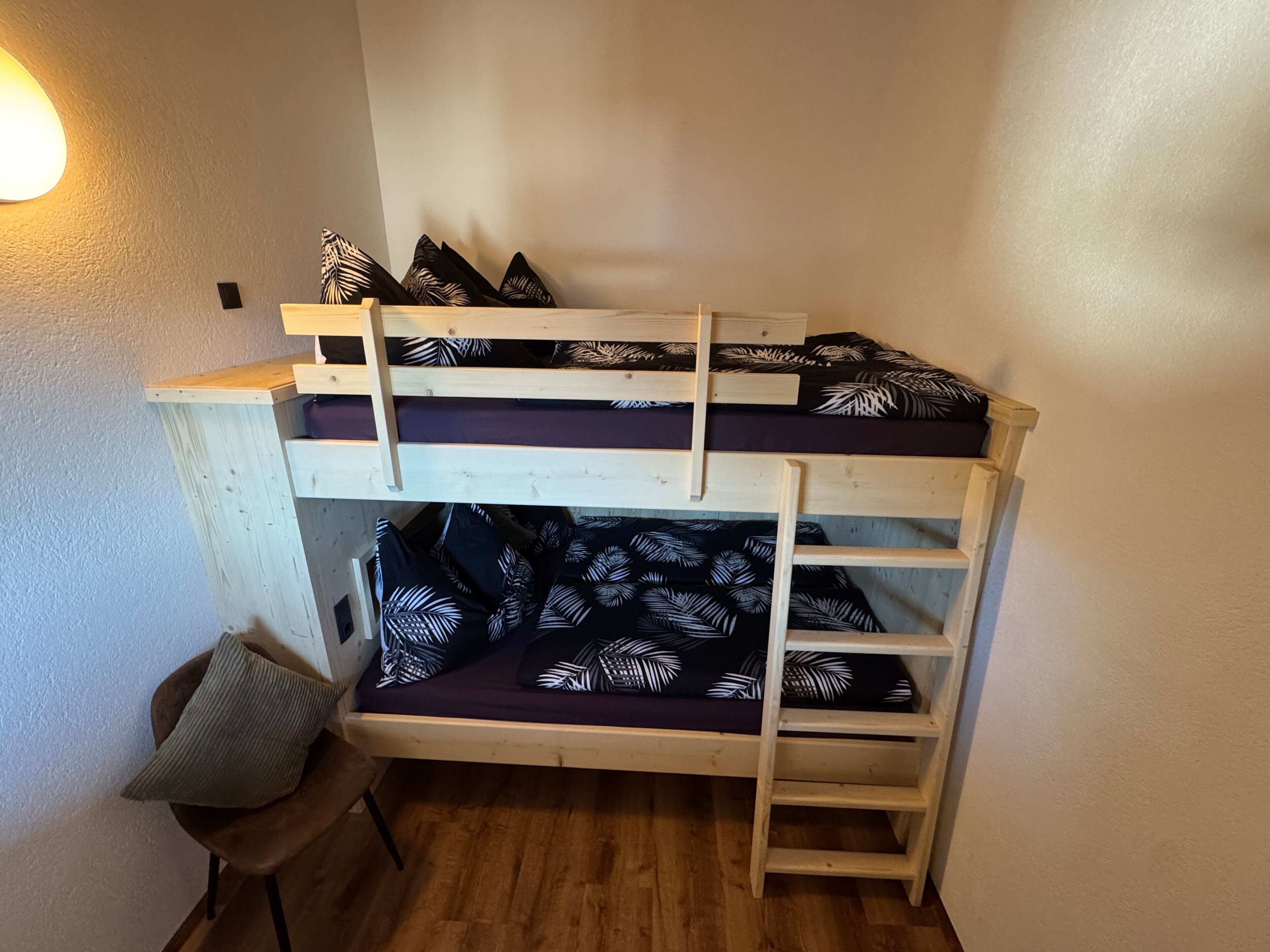 A bunk bed with a ladder, a chair, and a wall-mounted light fixture.