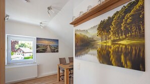 Een kamer met een eettafel, stoelen, een raam en een groot landschap op de muur.