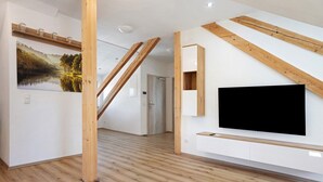 Een modern interieur met houten balken, een wandtelevisie en een groot landschap.