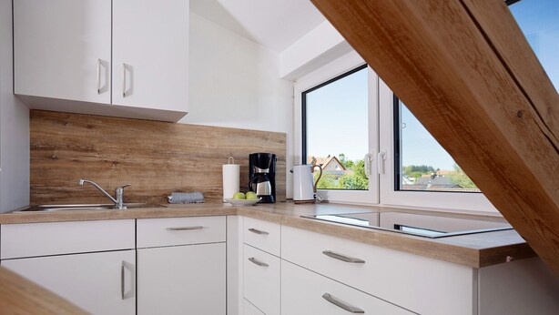 Een moderne keuken met witte kastjes, een houten aanrecht, een koffiezetapparaat en een raam met uitzicht op huizen.
