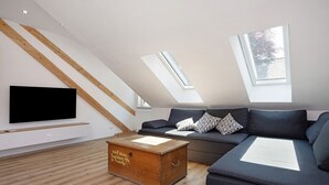 Een moderne woonkamer met een schuine kap, een ingebouwde televisie, een houten kist en een donkergrijze bank.
