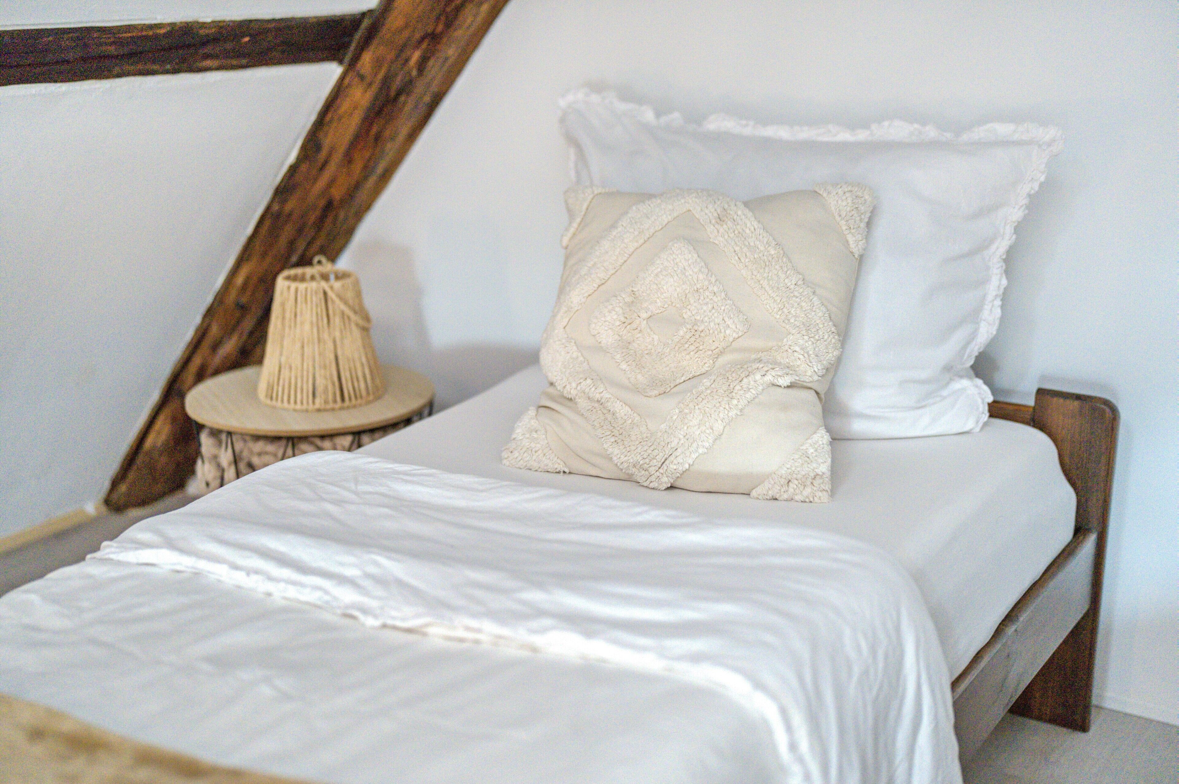 Een bed met witte lakens, een houten hoofdbord en een nachtkastje met een lamp.