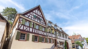A traditional half-timbered building with a staircase leading to the entrance, a visible fire hydrant, and a clear sky.