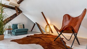 A cozy loft bedroom with a sloped ceiling, a leather chair, a blue sofa, a shaggy rug, and a lamp.