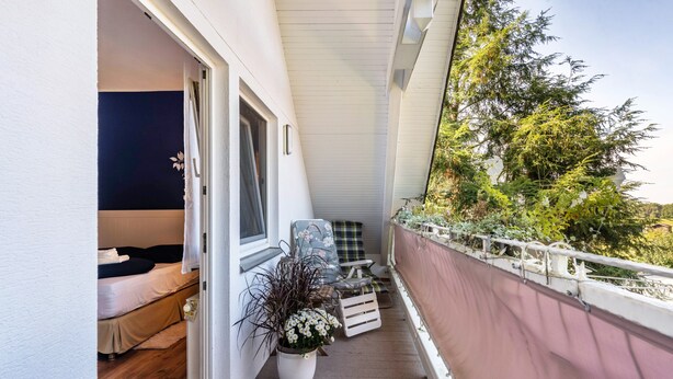 Un balcon avec un lit, une chaise, un pot de fleurs et une vue sur les arbres.