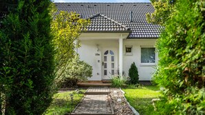 Une maison avec un toit en tuiles, une façade blanche et le numéro « 19a » sur la porte. Un chemin pavé mène à l’entrée.