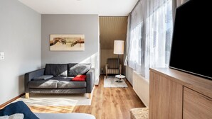 Un salon moderne avec un canapé, un téléviseur à écran plat, une lampe et un tableau accroché au mur.