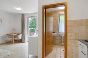 Una habitación moderna con comedor, baño con lavamanos y radiador, y vistas al exterior con vegetación.