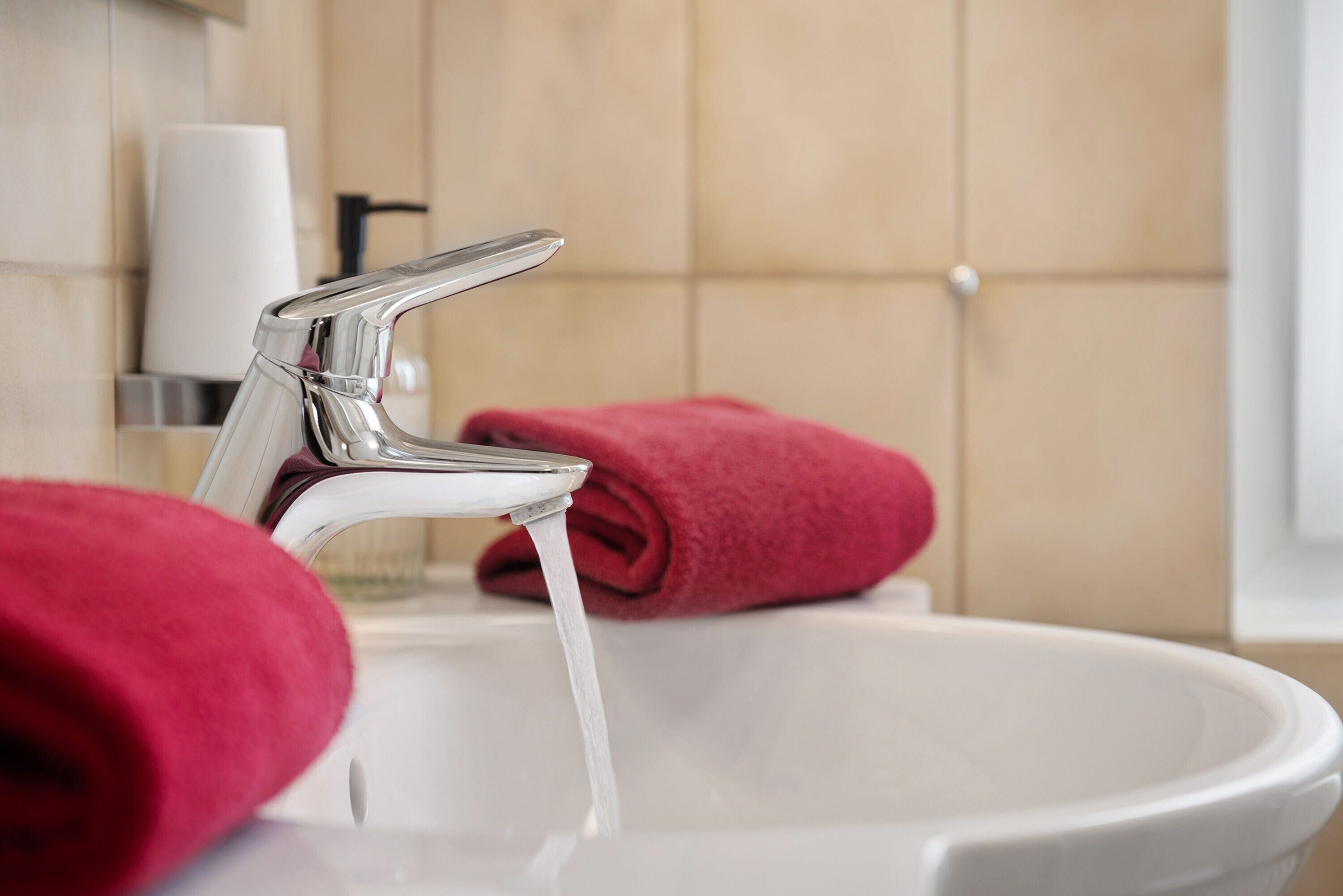 A bathroom with a white sink, chrome faucet, and a rolled-up red towel.