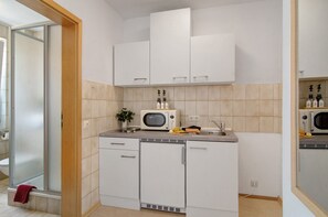 Cocina compacta con alacenas blancas, microondas, pileta y una mesada pequeña.