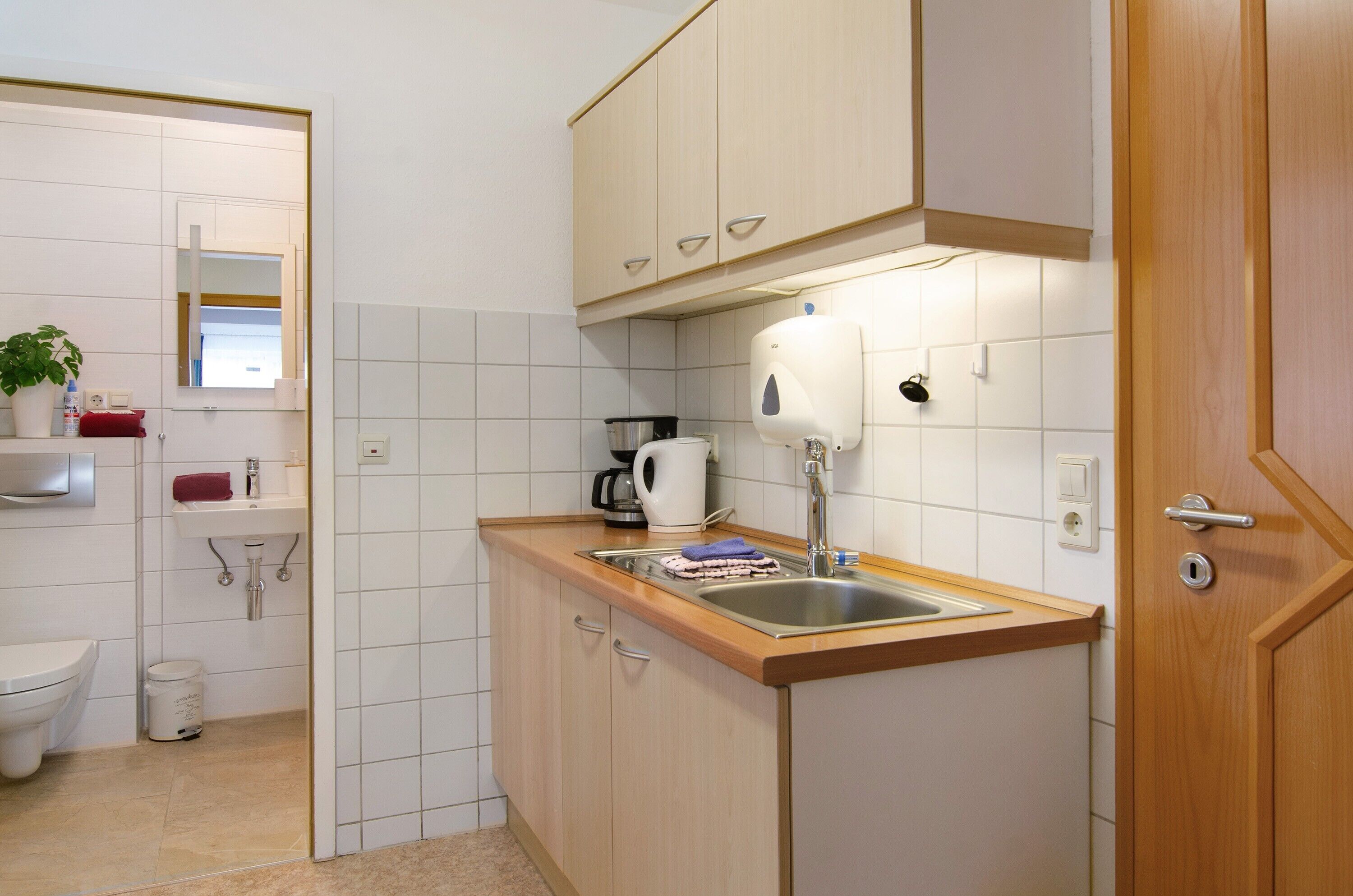 Una cucina compatta con lavandino, macchina del caffè e specchio.