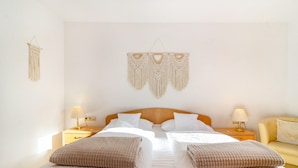 A double bed with a wooden headboard, two bedside tables with lamps, a wall hanging, and a sofa.