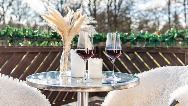 A round table with two wine glasses, a candle, and decorative pampas grass.