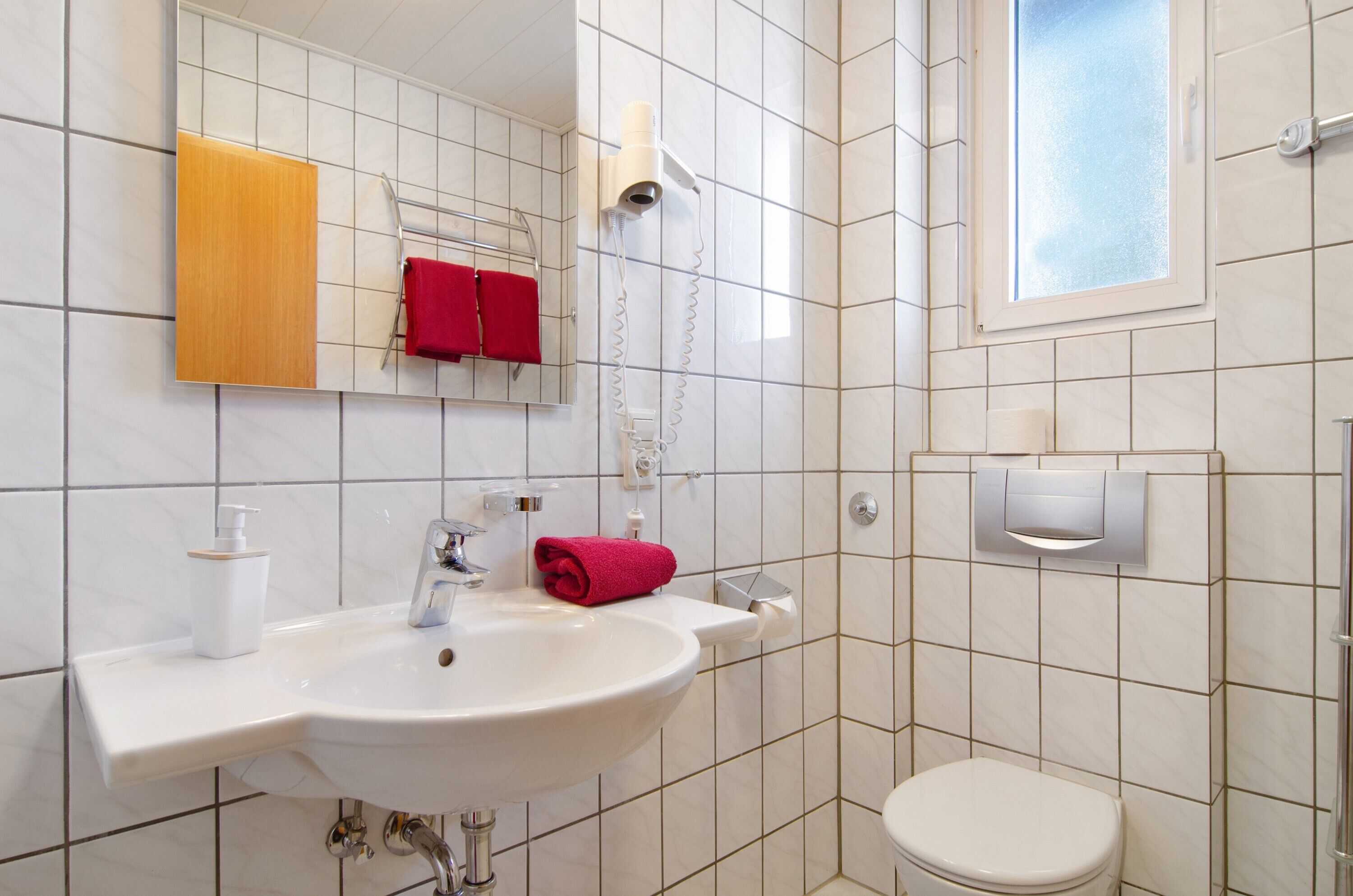 Un baño con lavamanos, espejo, toallero y retrete.