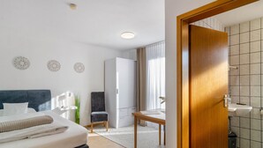 A hotel room with a bed, a desk, a chair, a wardrobe, and a bathroom with a sink and toilet. - Studio Apartment 'Nr 6' with Shared Terrace, Shared Garden and Wi-Fi (Bad Dürrheim)