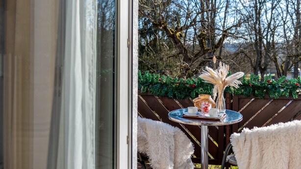A view through a glass door to an outdoor seating area with a round table, chairs, and a decorative vase. - Studio Apartment 'Nr 6' with Shared Terrace, Shared Garden and Wi-Fi (Bad Dürrheim)
