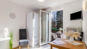 A modern room with a sliding glass door, a white wardrobe, a small table with a vase, and a mounted TV. - Studio Apartment 'Nr 6' with Shared Terrace, Shared Garden and Wi-Fi (Bad Dürrheim)