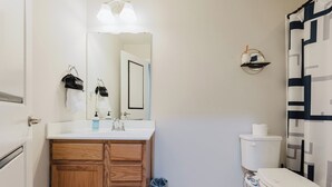 A bathroom with a wooden vanity, a white sink, a mirror, a toilet, and a shower curtain with a geometric pattern. - Unique 2D-Style Family Retreat (Pennsburg)