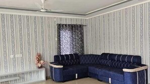 A spacious living room with a dark blue sectional sofa, a ceiling fan, and a decorative wall panel.