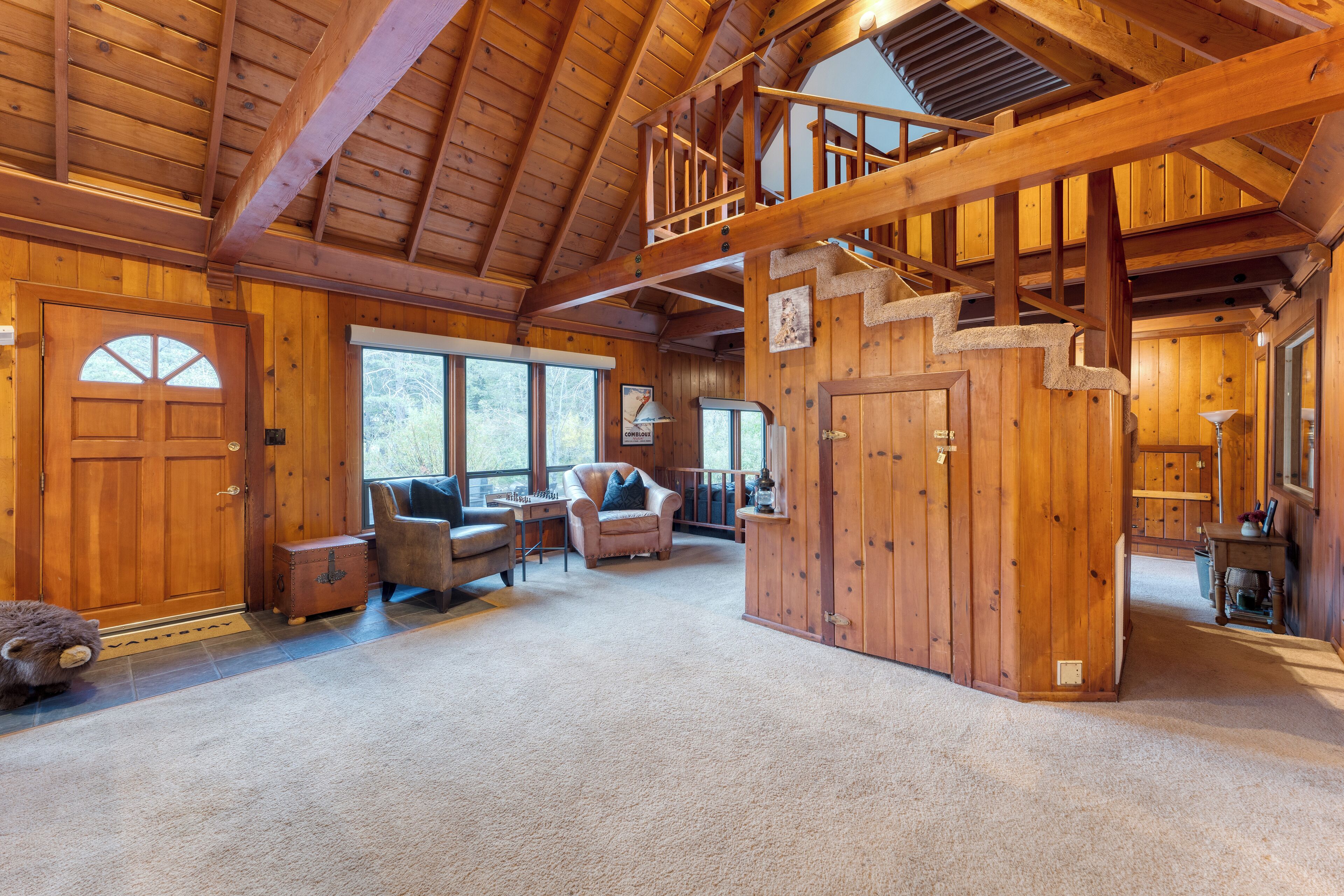 Une vaste cabane en rondins dotée d’un plafond haut, d’un escalier et d’un coin salon confortable avec une cheminée.
