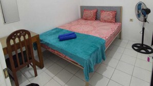 Una stanza piccola e pulita con un letto singolo, una sedia, una scrivania e un ventilatore.
