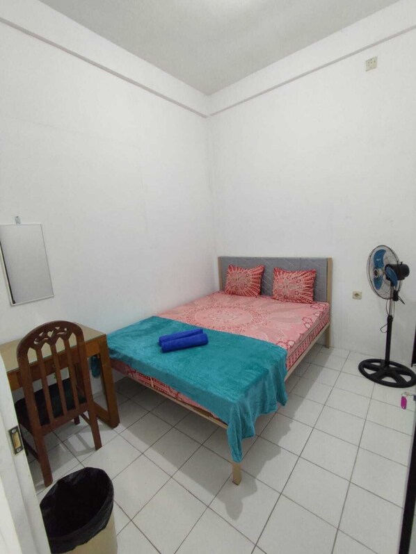 A small, clean room with a single bed, a chair, a desk, and a fan. - Hotel MK 27 (Surabaya)
