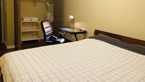 Ein Hotelzimmer mit Bett, Schreibtisch, Stuhl, Ventilator und Ablagefläche mit Handtüchern.