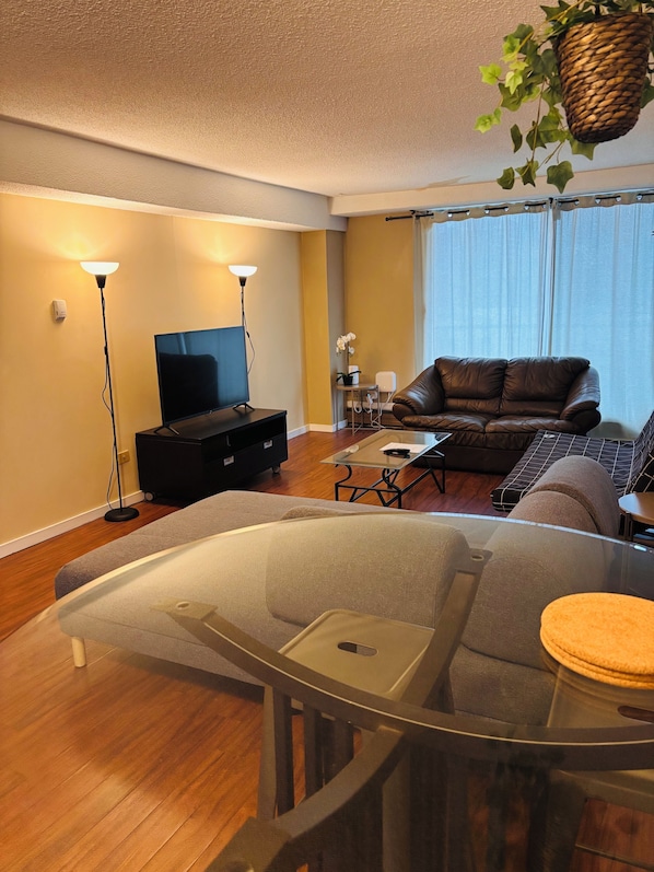 Una sala de estar moderna con una mesa de centro de vidrio, un sofá de cuero y un televisor de pantalla plana.