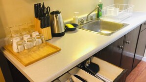 Eine Küche mit Spüle aus Edelstahl, Schneidebrett aus Holz und einer Schubladeneinsatz für Küchenutensilien.