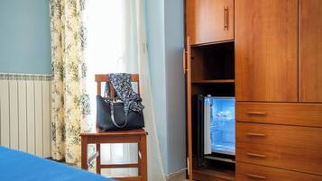 Una habitación con cama, un armario de madera, una mesita con un bolso y un refrigerador.