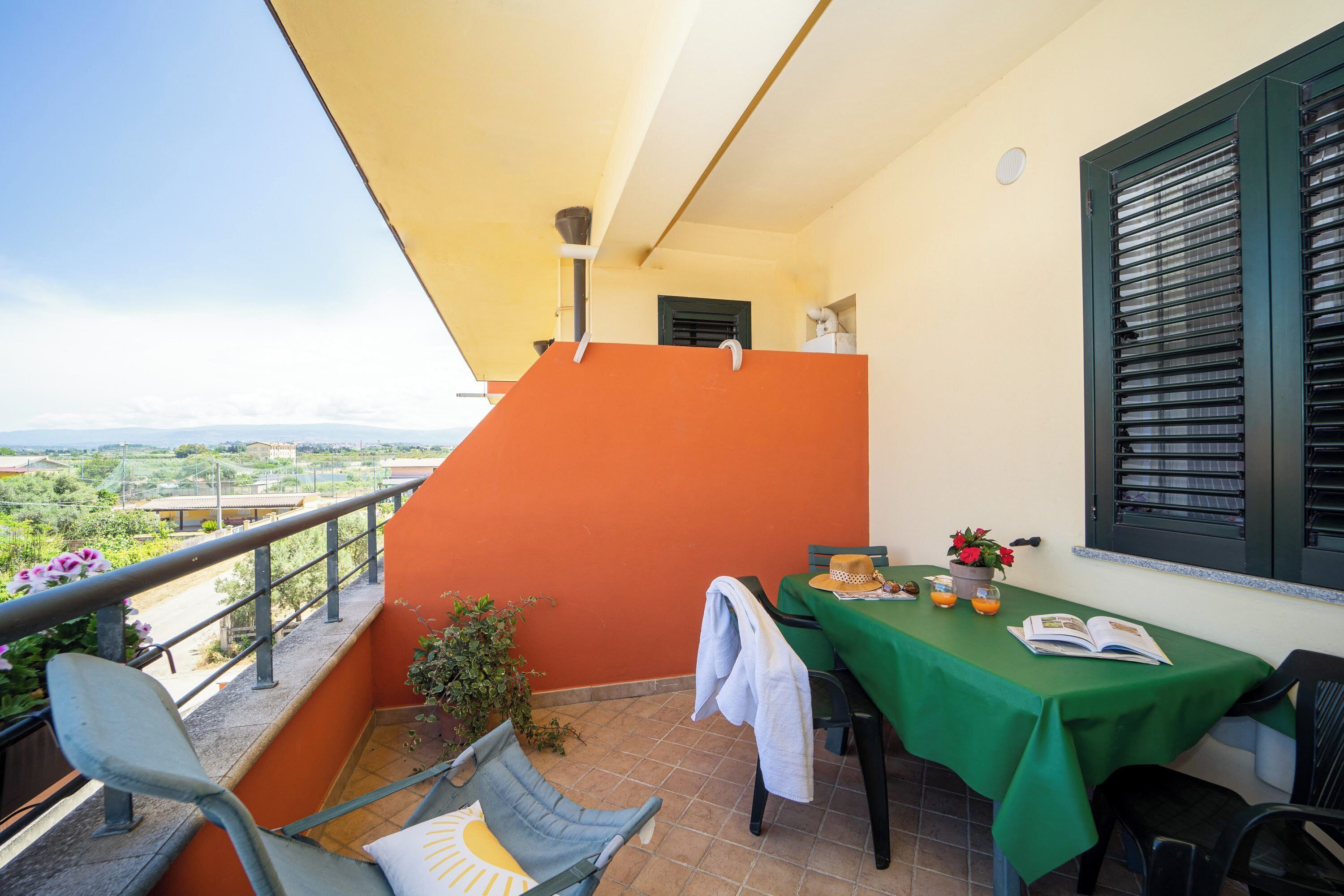 A balcony with a table set for two, a chair, and a view of the countryside.