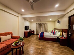 A hotel room with a bed, a desk with a TV, a sofa, and a small table with fruit. - Zip By Spree Hotels Kolhapur (Kolhapur)