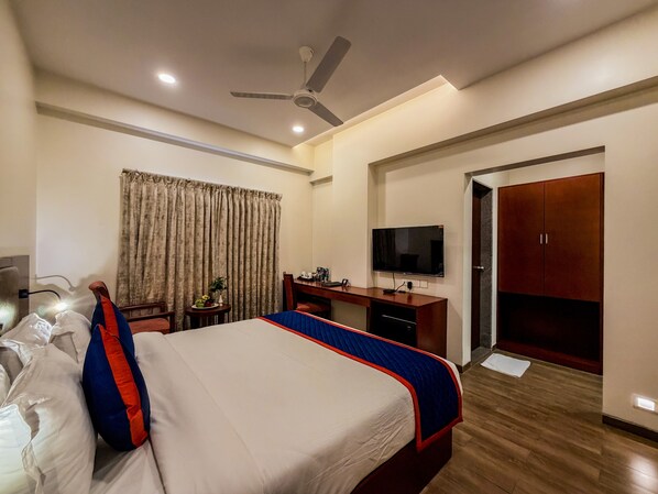 A hotel room with a bed, a desk, a TV, a wardrobe, and a ceiling fan. - Zip By Spree Hotels Kolhapur (Kolhapur)