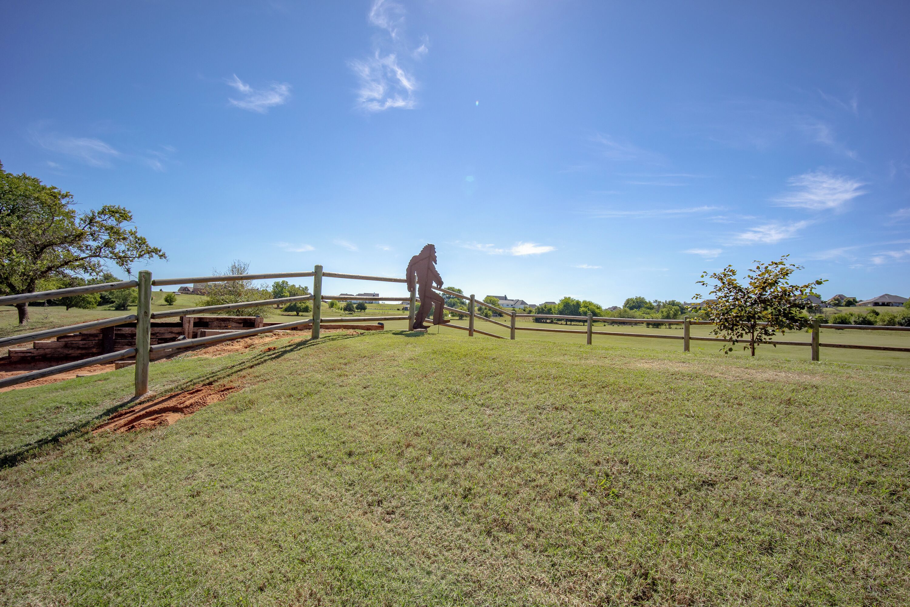 A person standing on a grassy hill with a wooden fence and a clear blue sky.