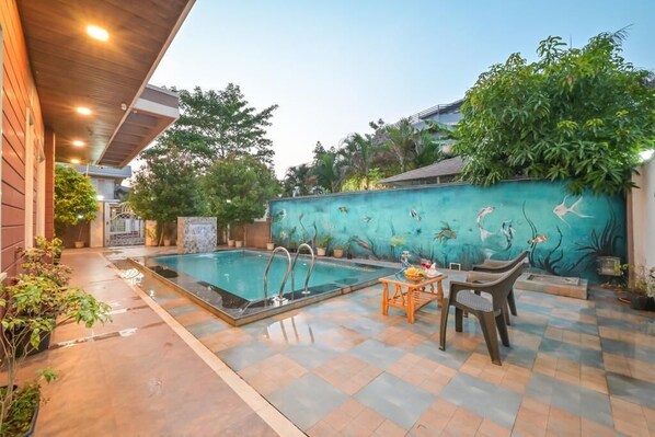 A swimming pool with a mural of fish on the wall, a table with chairs, and potted plants around the area.
