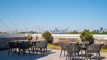 An outdoor patio with round tables and chairs, a brick wall, and a view of a city skyline.
