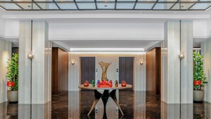 Un moderno hall de hotel con piso de mármol pulido, una mesa redonda central decorada y lámparas simétricas.