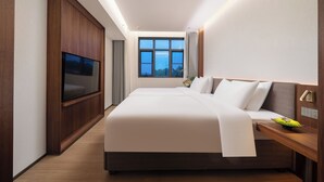 Habitación de hotel con una cama grande, televisión de pantalla plana, ventana con cortinas y cabecero de madera.