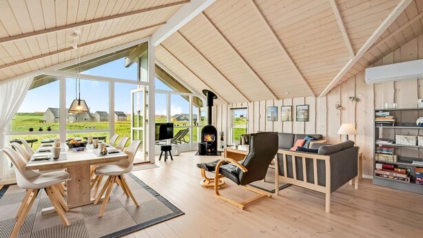 Una habitación amplia con techo alto, ventanas grandes, chimenea, zona de comedor y estantería.