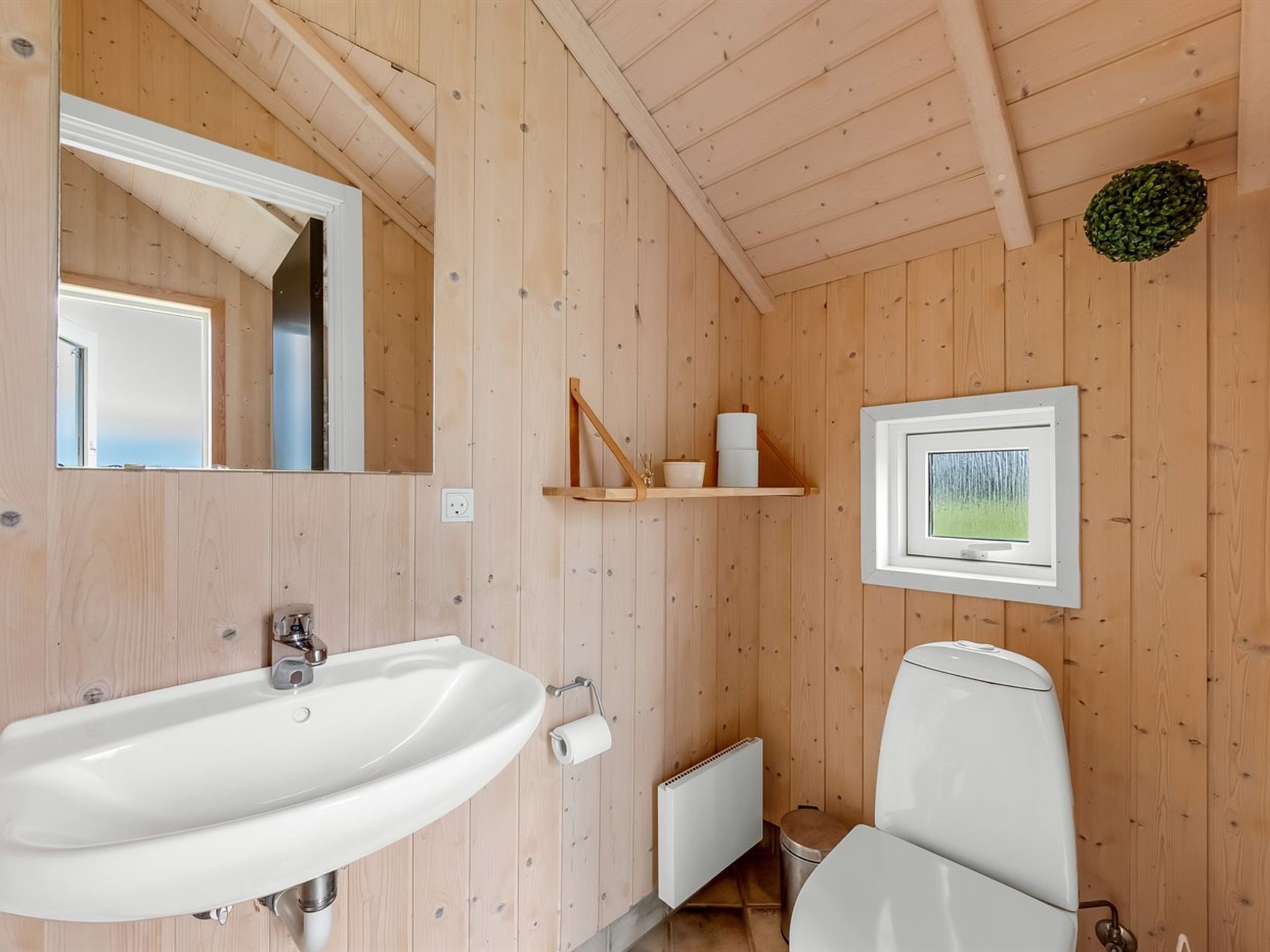 Ein Badezimmer mit Holzwandverkleidung, einem weißen Waschbecken, einer Toilette und einem gerahmten Bild an der Wand.