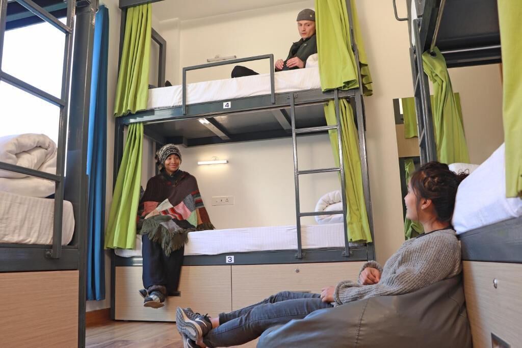 Een slaapzaal met stapelbedden, genummerde bedden en groene gordijnen.